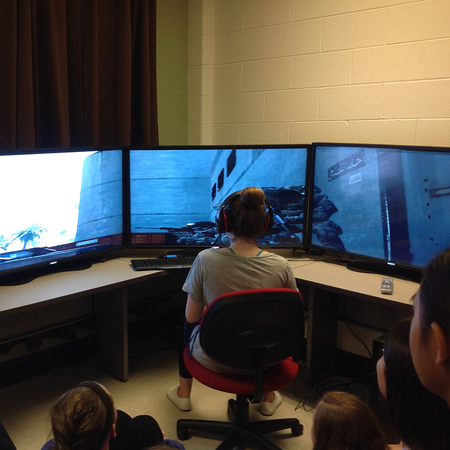 student in front of three computer monitors