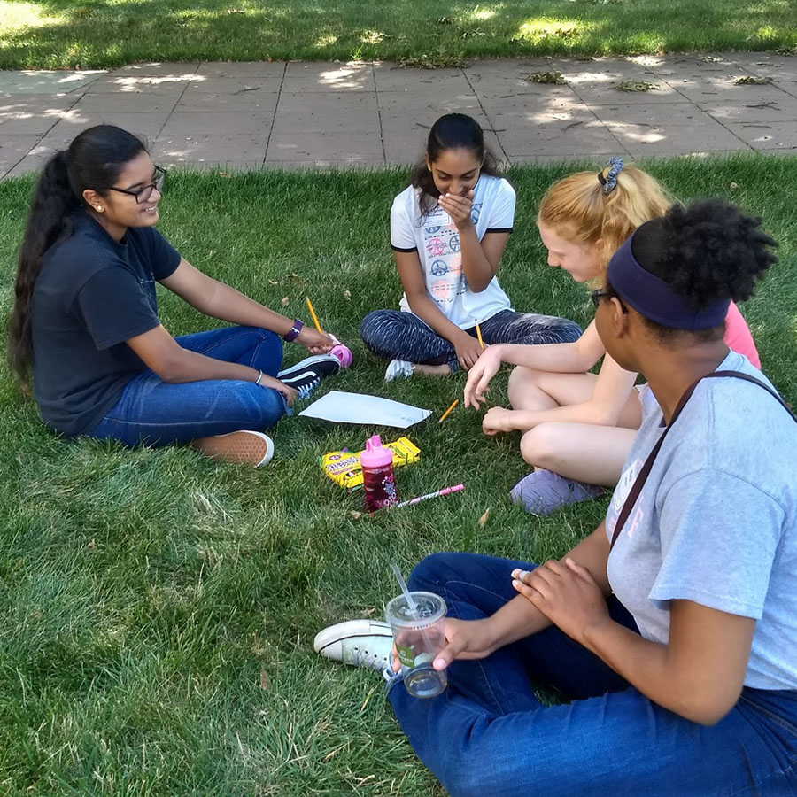 three students and a mentor sitting outside on grass