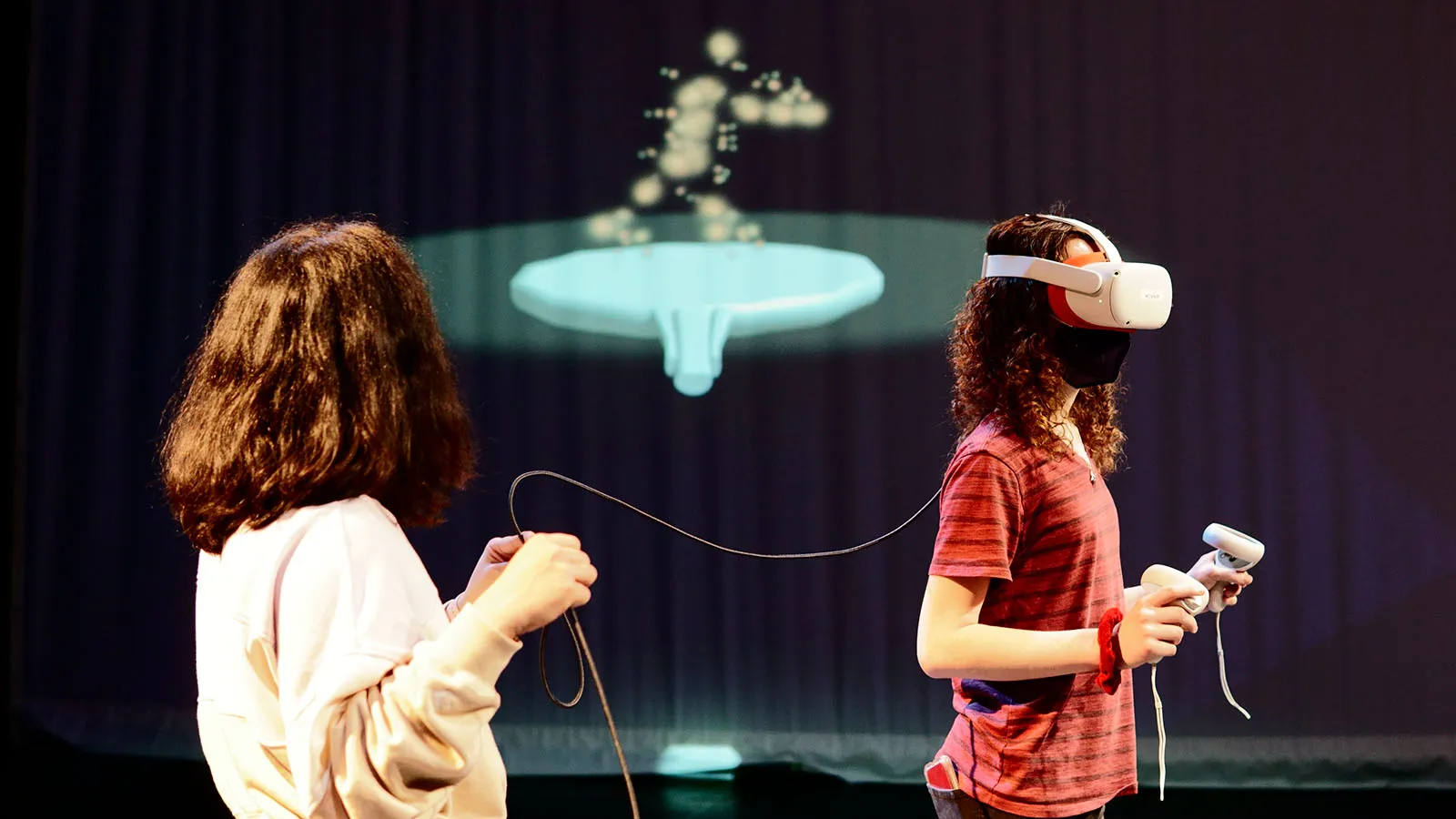 Two people engage in a VR experience with a projection in the background