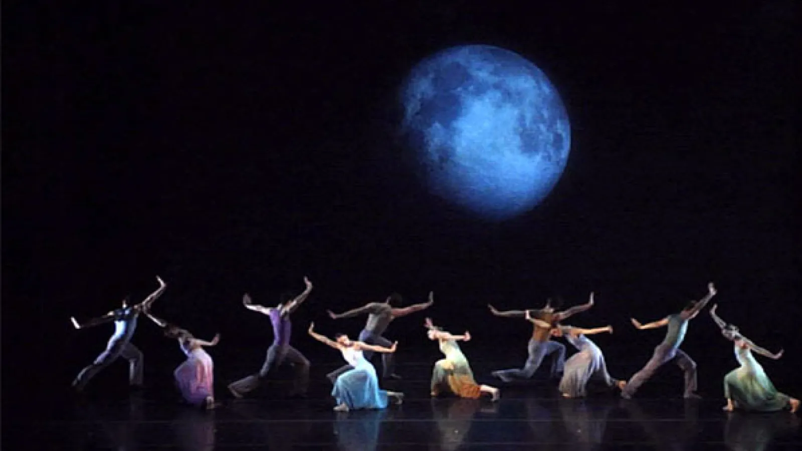 Dancers performing in front of a large screen with digital projection of the moon