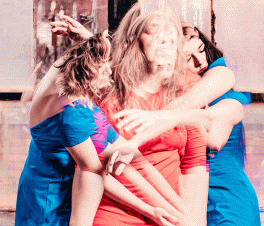 A still shot from a dance project related to Livable Futures. Three women are shown in the middle of a dance. The woman in the middle is being embraced by the women on either side of her.
