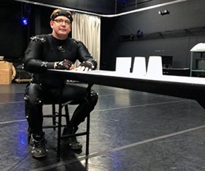 Kellen wearing a motion capture suit sitting at a table