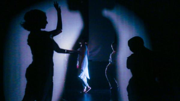 Dancers shadows, sihouettes, and live bodies are juxtaposed around light and a semi transparent scrim 