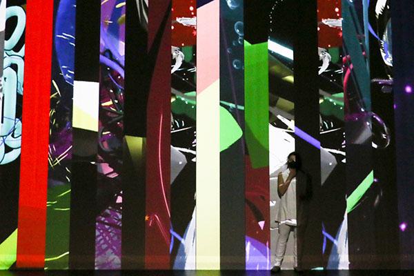A dancer dressed white stands in front of a screen with many vertical slices of different video projections fill the space 