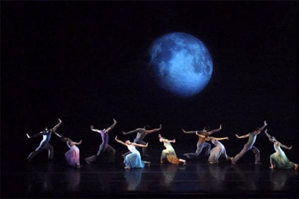 Dancers performing in front of a large screen with digital projection of the moon