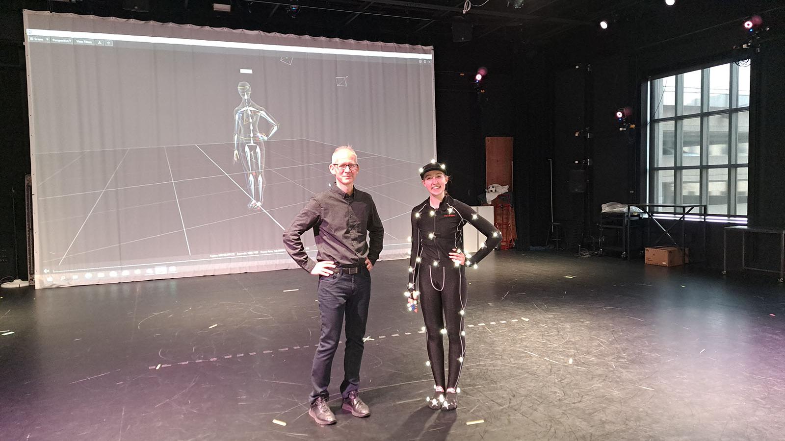 Wobbe and dancer Vivian Corey smile and pose with hands on their hips in from of a motion capture projection
